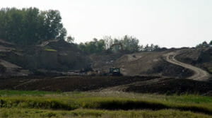 Hills of dirt with heavy earth-moving equipment in background.