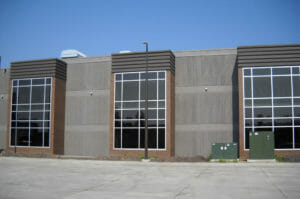 Two-story gray concrete and brown-bricked building with three jut-outs of windows.