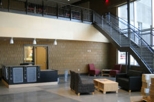 Interior atrium of Bisek Hall at NDSCS with metal staircase curved around curved two-story wall of windows to the right leading to upstairs seating area.