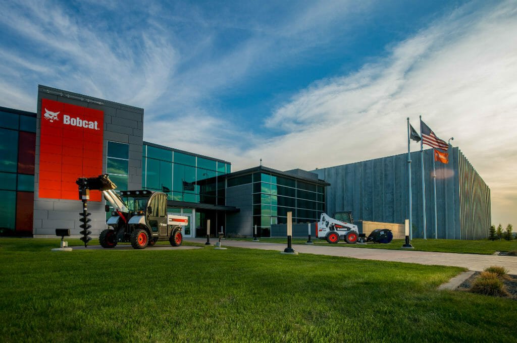 Exterior view of Bobcat building at unset with lush green grass and bobcat equipment displayed on lawn.