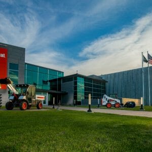 Exterior view of Bobcat building at unset with lush green grass and bobcat equipment displayed on lawn.