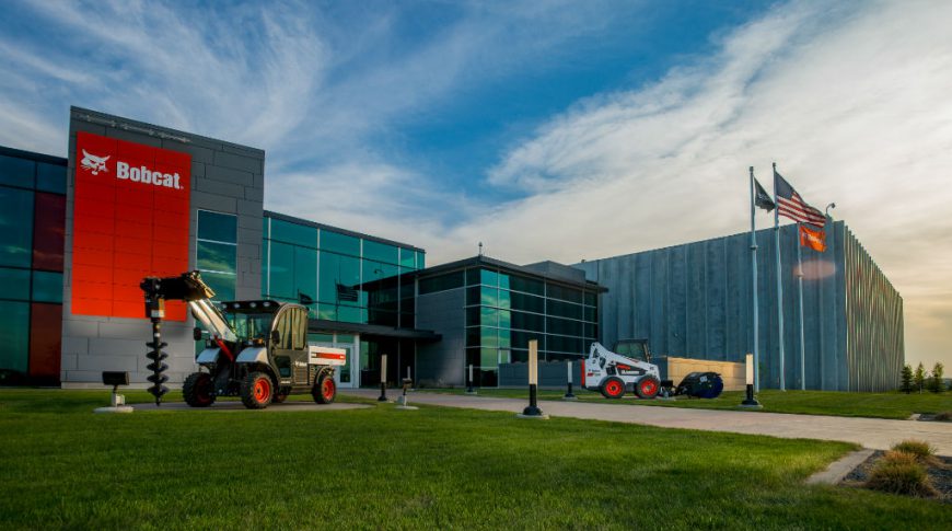 Bobcat Acceleration Center-P-Ext1-1024x680-Commercial Construction Exterior view of Bobcat building at unset with lush green grass and bobcat equipment displayed on lawn.