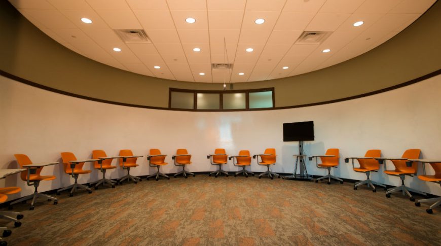 Bobcat Acceleration Center-P-Int2-1024x680-Commercial Construction Round room with green and orange carpet tiles, orange desk chairs on back wall with round whiteboard on entirety of rounded wall.