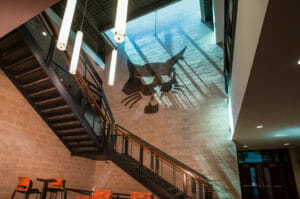 Brick wall two-story opening with black metal staircase to second floor and bobcat metal emblem on back wall.