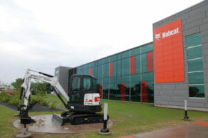 Exterior of gray and red tiled Bobcat Acceleration building with bobcat machine on display in the foreground.