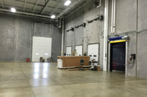 Interior warehouse with four truck garage doors and concrete walls and floors with exposed ceiling.