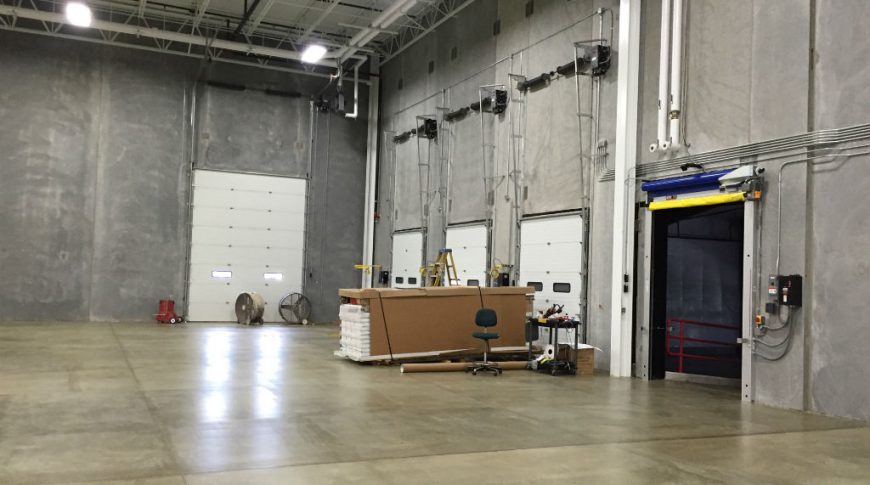 ComDel Innovation 1Exp-Int1-edit-Commercial Construction Interior warehouse with four truck garage doors and concrete walls and floors with exposed ceiling.
