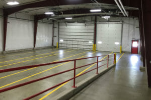Interior building with exposed large dark maroon arched beams holding up the structure, concrete floor and two large truck bays.