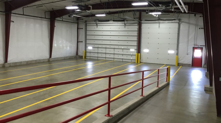 ComDel Innovation 1Exp-Int3-edit-Commercial Construction Interior building with exposed large dark maroon arched beams holding up the structure, concrete floor and two large truck bays.