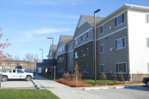 Exterior corner view from parking lot of three-story beige and brown bricked residence building with parking lot on each side.