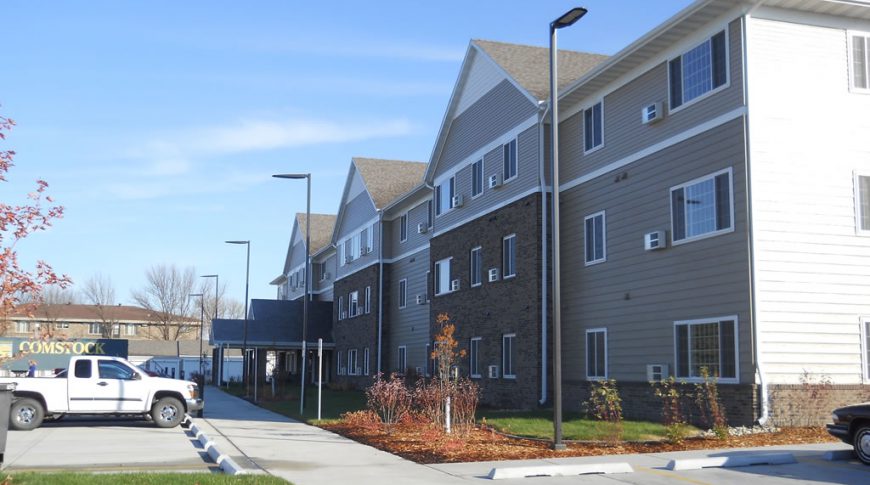 Exterior corner view from parking lot of three-story beige and brown bricked residence building with parking lot on each side.