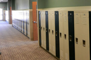 Locker hallway with alternating beige and black lockers with green accent walls above and brown and beige carpeting beneath. Classroom door entrances every so many lockers.