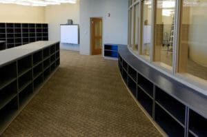 Beige and brown carpeted room with beige walls and storage cubies throughout. Half wall of cubies on right side with arched wall of windows above.