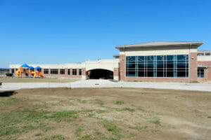 Exterior view of entrance to Dickinson's Prairie Rose Elementary school with wall of two-story high windows to the right and playground area to the left.