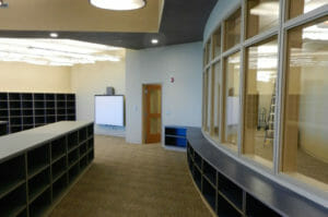 Gray room with cubies in middle, tall cubbies in the back left, and low cubbies in the right along a curved wall of windows.