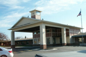 Large awning over drive up to yellow sided building with brown shingles accent.