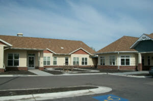 Yellow sided building with red siding accents and brown shingles with white trim around windows. Unfinished landscaping pathways in front of building.