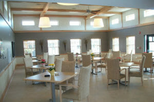 Large open room with two stories of windows and gray and light gray accent walls with light millwork throughout. Square tables and chairs throughout the room.
