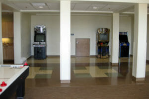 Game room at Minot Air Force Base F08 dormitory with arcade games to the back wall and glimpse of air hockey table in left foreground.