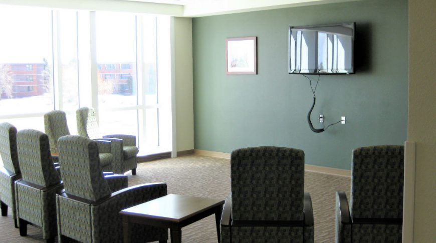 Lounge room with chairs and side tables looking toward accent green wall with big-screen tv.