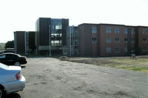 Unfinished brown metal panel exterior of three-story building college residence hall with unfinished parking lot in front.