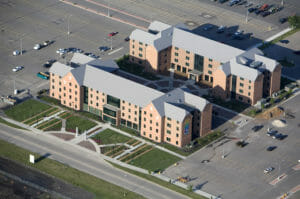 Aerial view of NDSU Living Learning Center buildings with red brick and gray metal roofing surrounded by lush green and flower courtyards to the buildings' fronts.