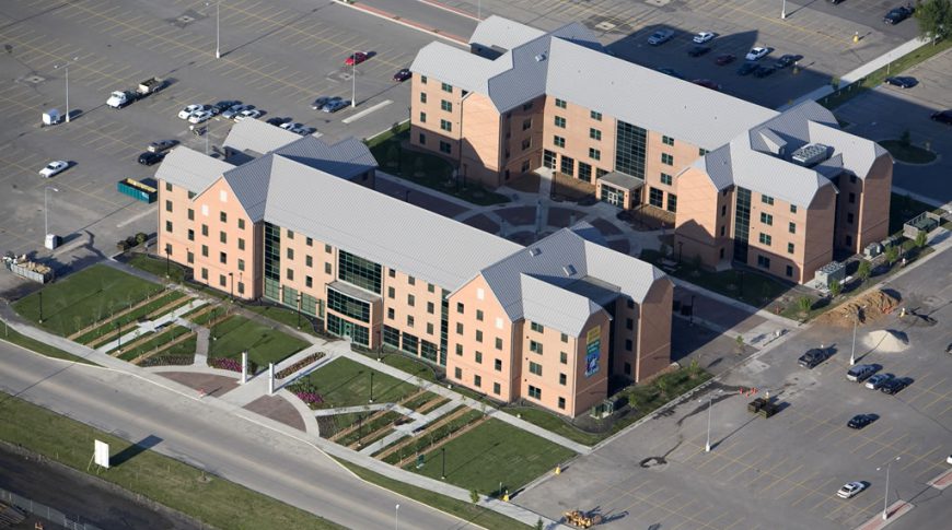 Aerial view of NDSU Living Learning Center buildings with red brick and gray metal roofing surrounded by lush green and flower courtyards to the buildings' fronts.