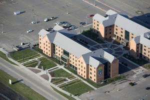 Aerial view of NDSU Living Learning Center buildings with red brick and gray metal roofing surrounded by lush green and flower courtyards to the buildings' fronts.