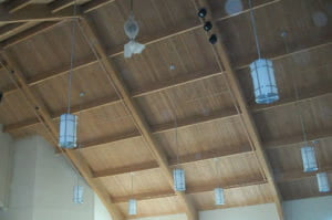 A-frame ceiling paneled in natural pine wood with wooden rafters exposes and modern lights hanging down.