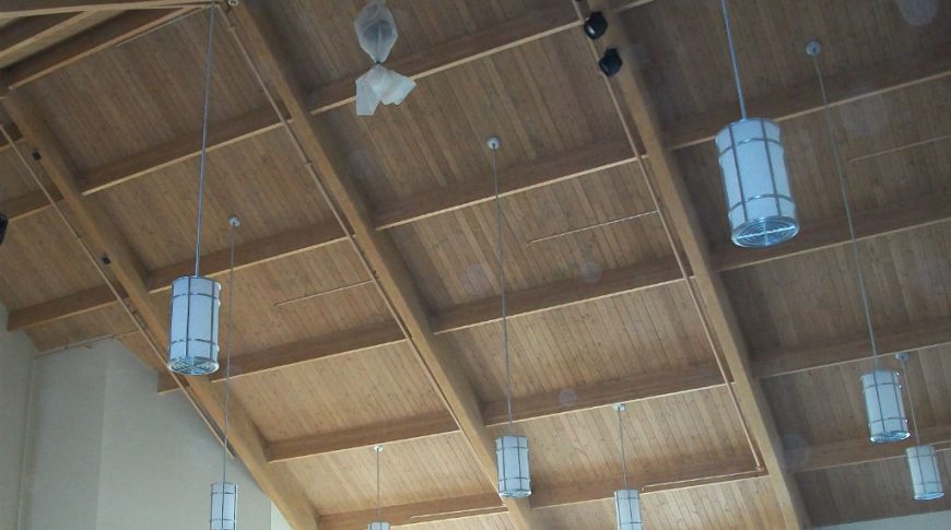 A-frame ceiling paneled in natural pine wood with wooden rafters exposes and modern lights hanging down.