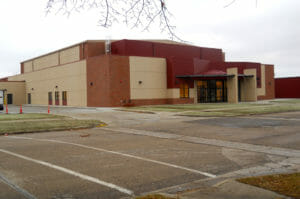 Exterior view of beige concrete and red bricked school building as seen from across the street.