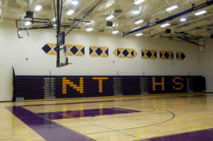 Gymnasium with unfurled purple bleachers to the back wall with the letters "NTHS" in yellow.