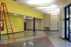 Entrance area to New Town High School with bright yellow accent wall and purple accent column and lights. Tall red a-frame ladder in the foreground.