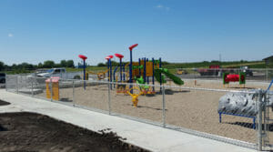 Four-foot chain-link fence enclosure with blue, red, green, and yellow playground equipment inside.