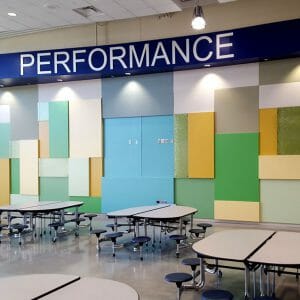 Interior two-story tall accent wall with the word "PERFORMANCE" at the top with panels of light blue, green, yellow, and gray underneath.