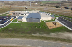 Side aerial view of Rothsay Public School with playground area to right foreground, school to center and parking lot to the left. Highway can be seen in background.