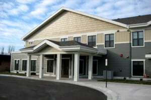Entrance with wooden gable to assisted living home with asphalt drive-up.