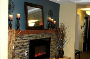 Tiled fireplace with dark blue-gray wall behind with mirror on mantle and candles and decorations flanking each side.