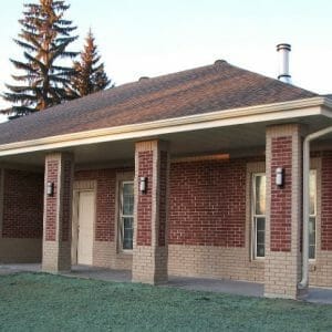Exterior of red and beige brick building with dark gray roof and new grass seed in front.