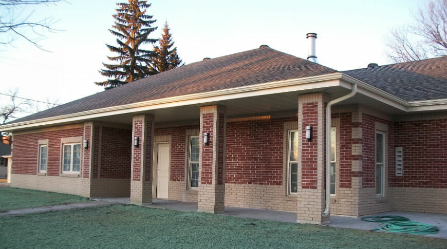 Exterior of red and beige brick building with dark gray roof and new grass seed in front.