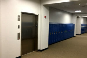 Interior of school locker hallway with blue lockers to the back wall and elevator to the back wall on the left.