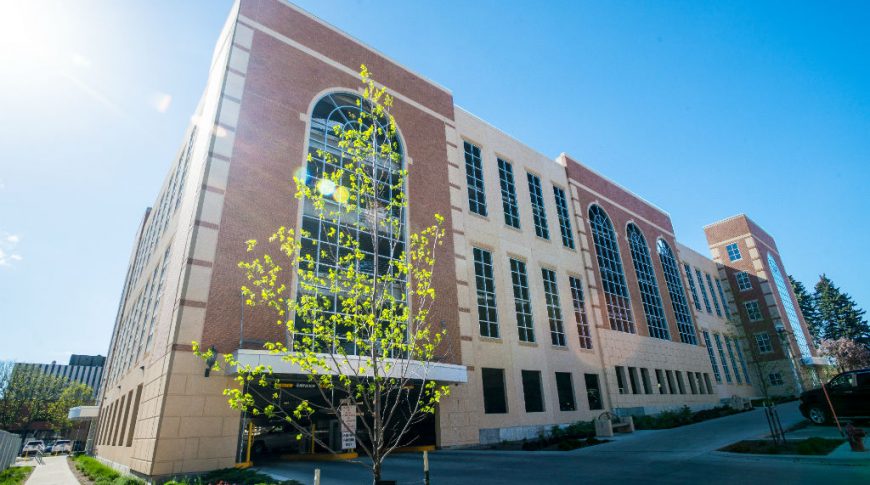 6th St. Parking Ramp-P-Ext1-1024x680-Government Construction Corner sidewalk view of beige brick and concrete building façade with windows throughout that hides a parking ramp behind.