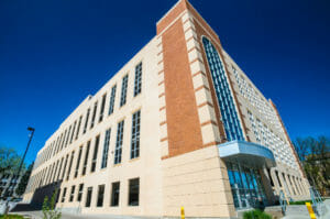 Brick and concrete building with large tall windows and slight entryway awning over glass covered doors.