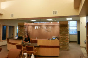 Light wooden reception desk with brown wall behind with Bremer Bank logo in silver flanked by two stone columns.