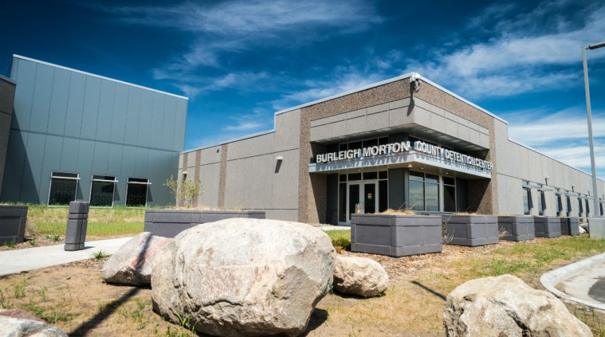 Burleigh Morton Detention Center-P-Ext1-1024x680-Government Construction Exterior of Burleigh Morton County Detention Center with gray concrete planter boxes around the side of the building and landscaping large boulders in front.