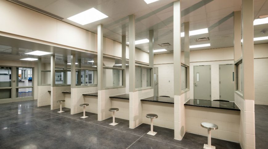 Burleigh Morton Detention Center-P-Int5-1024x680-Government Construction Visiting area at jail with six stations of one stool on each side of countertop with dividing glass between each section.
