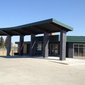 Black-tiled and red brick exterior of building with drive up-green-covered awning.