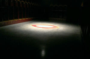Dimly lit Concordia locker room with spotlight on concrete floor with the C logo and glimpses of maroon and gold lockers around the edges.