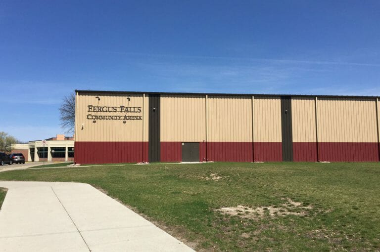 Exterior light brown, red, and dark brown metal building with words "Fergus Falls Community Arena" in metal sign.