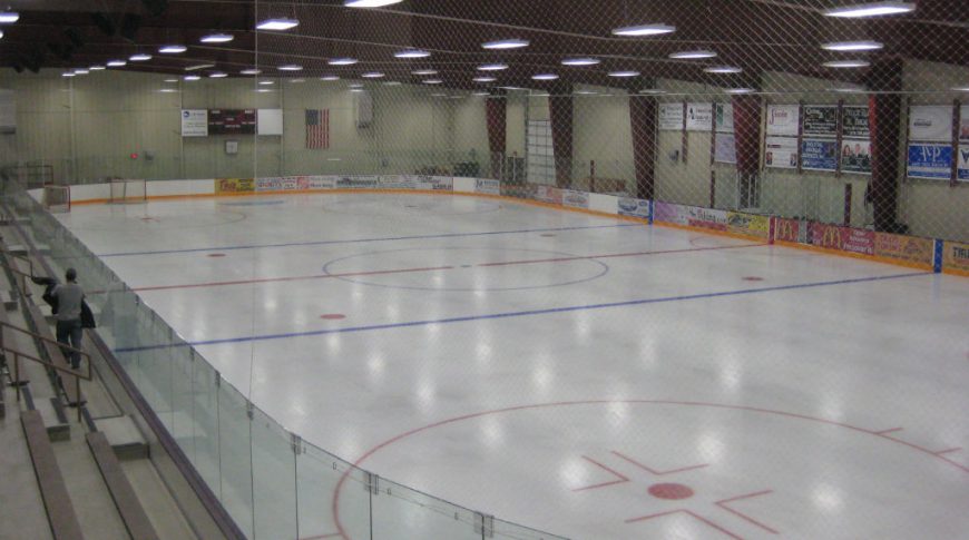 Ice hockey arena with floor-to-ceiling netting behind goals and business banners sprinkled throughout.